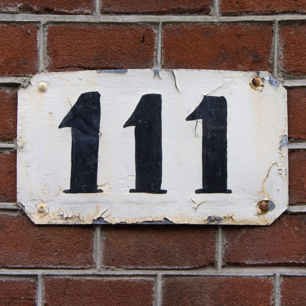 Number 111 on a metal plate nailed on a red brick wall