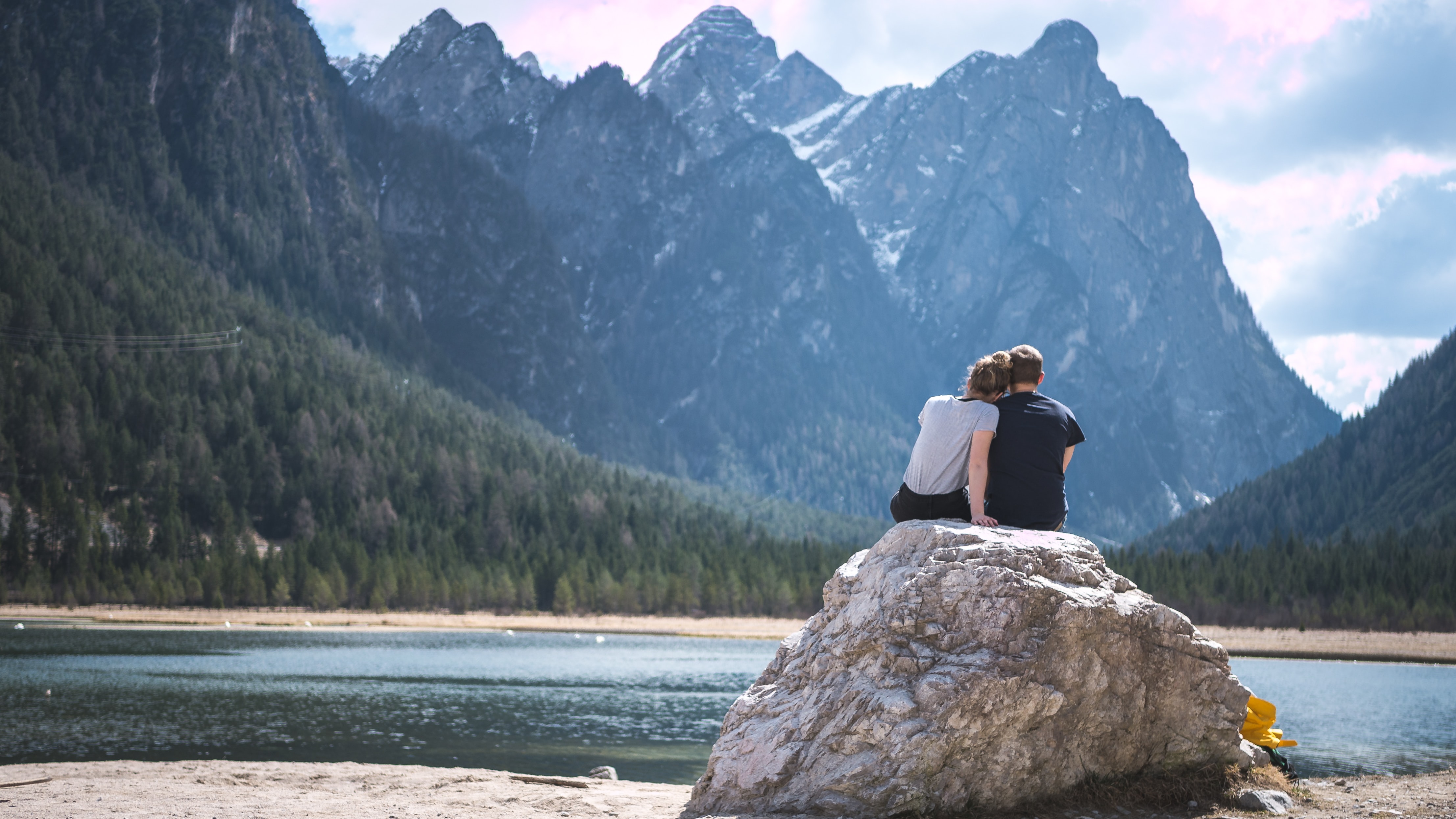A couple sites on a rock looking out over a lake
