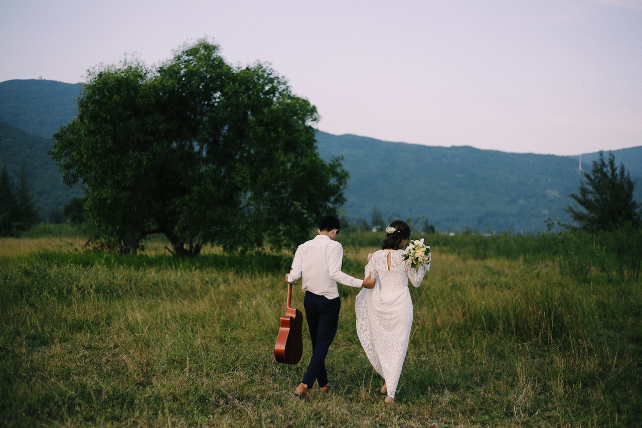Bride and Groom Walking in Grassy Field