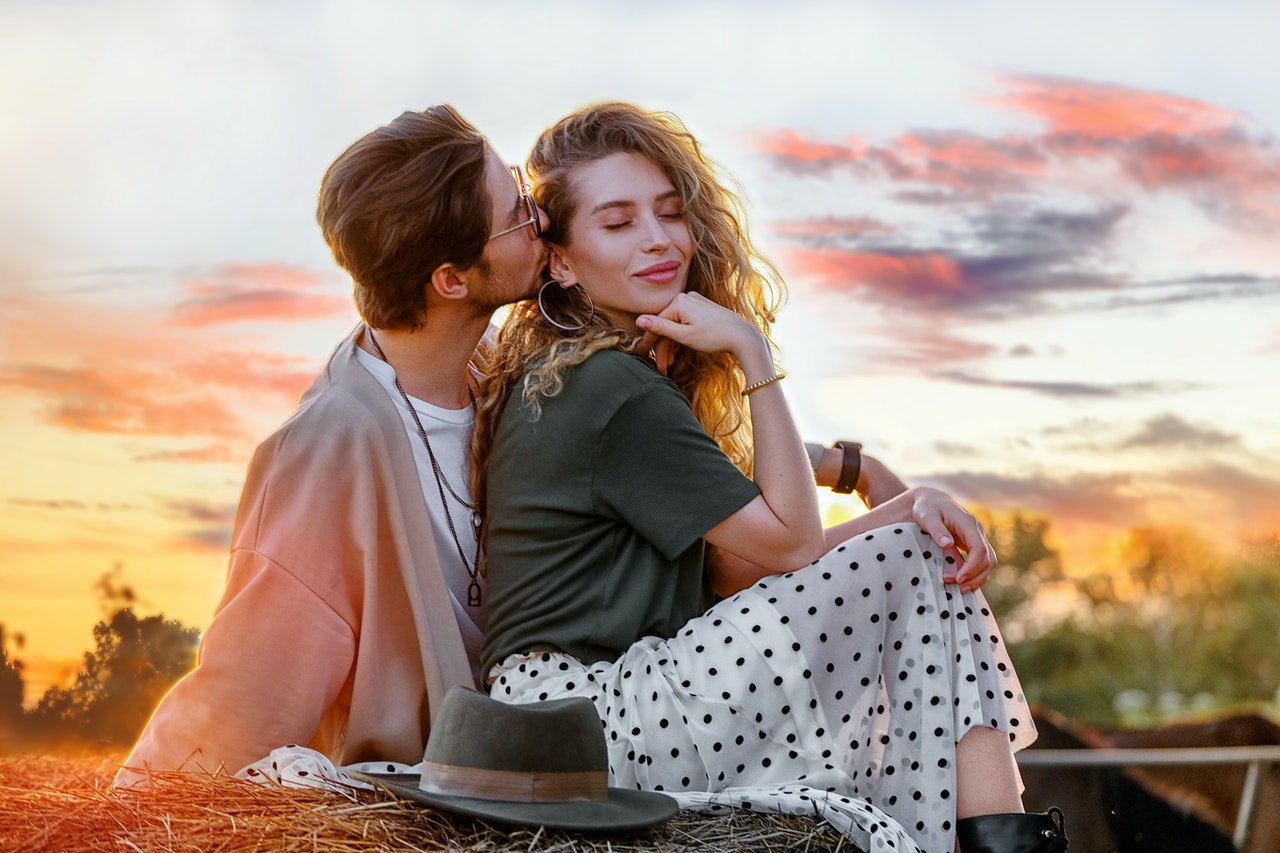 A man kissing his attractive girlfriend on haystack at sunset