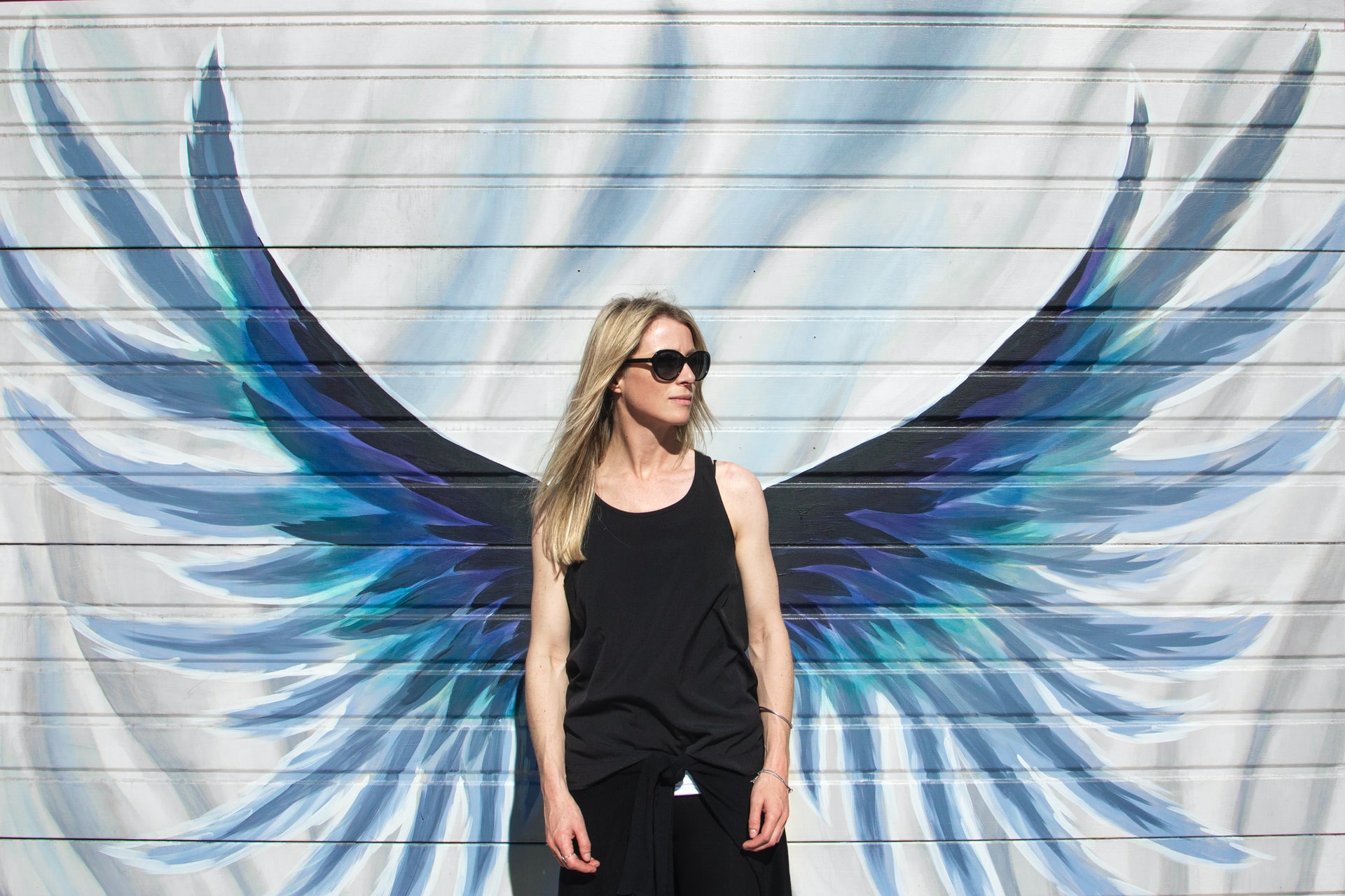 Women In Black Cloth Against Wall With Blue Angel Wings Painting