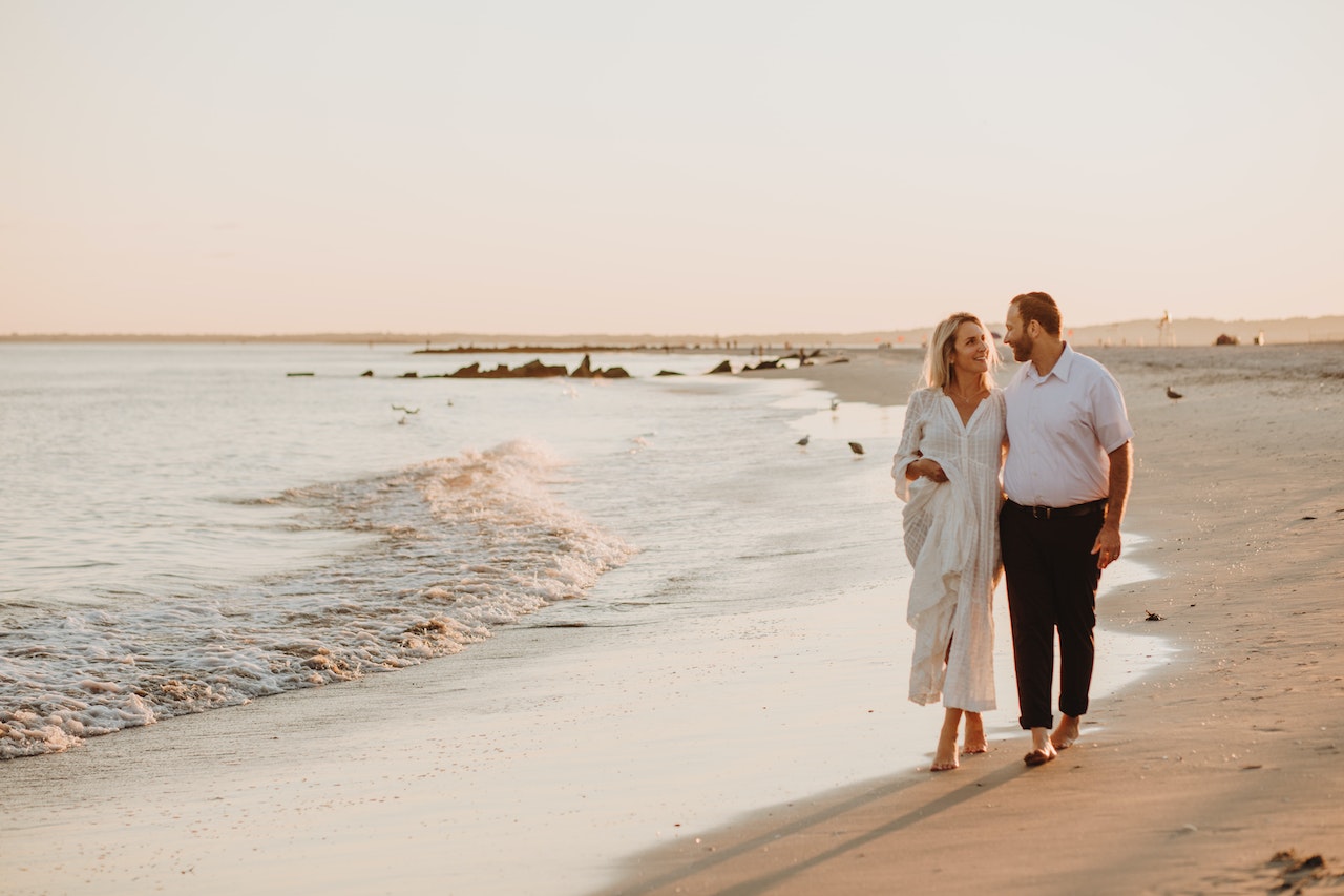 A Couple Walking While Looking At Each Other On The Beach Shore