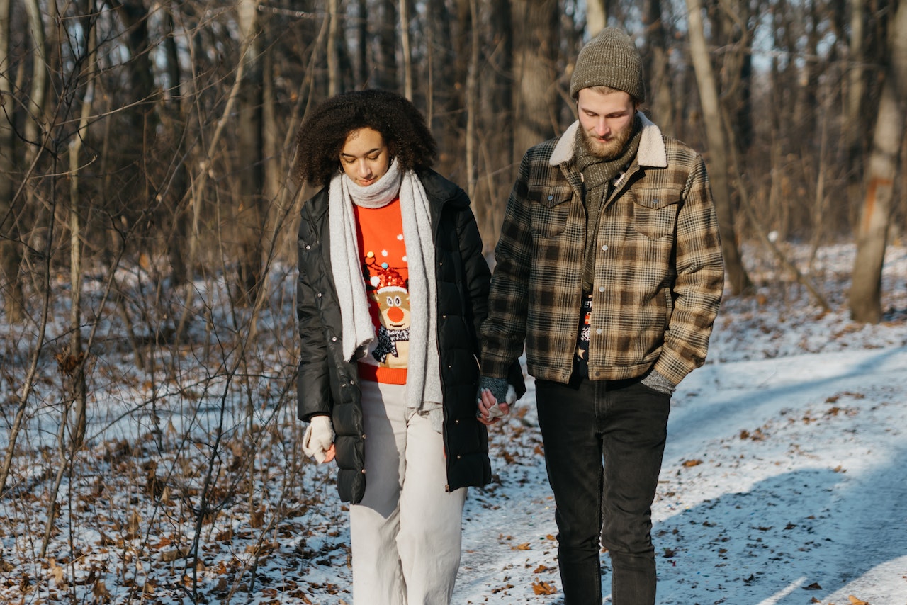 Couple Walking on Snow Covered Ground Near Trees, Holding Hands