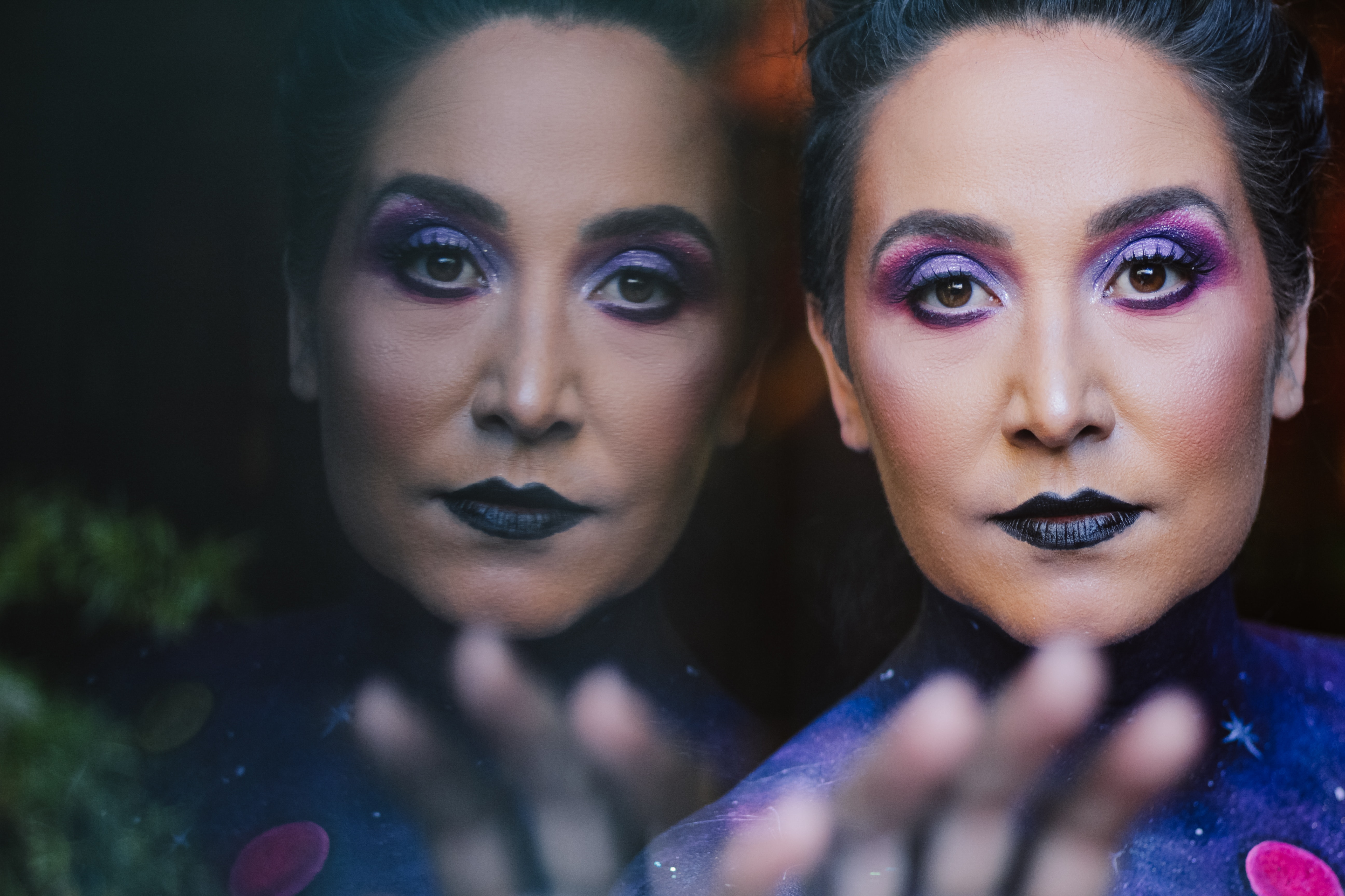 A woman with purple makeup and her reflection.