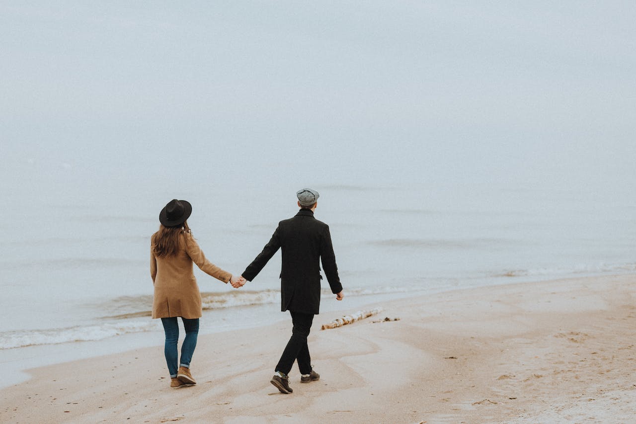 Man and Woman Holding Hands While Walking on Shore