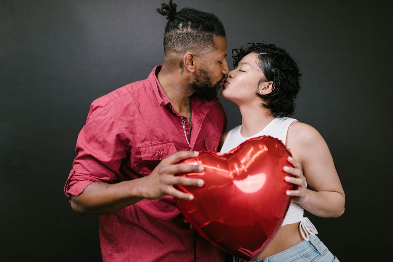 Couple Kissing While Holding a Red Heart Shaped Balloon