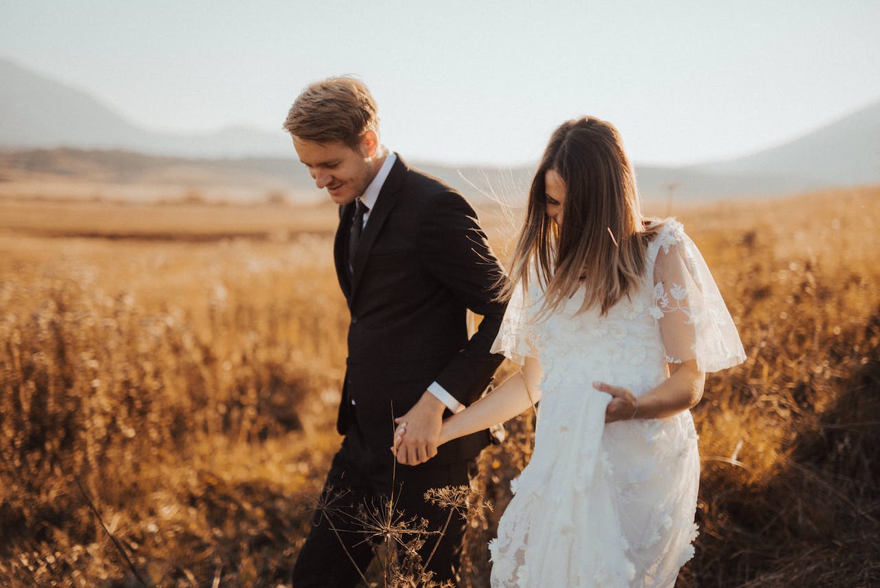 Man in Black Formal Suit Holding Woman's Hand in White Dress
